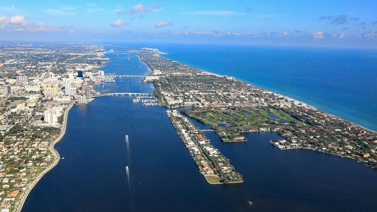 Aerial view of a coastal city with dense urban areas bordering a clear blue ocean, intersected by waterways and connected by several bridges.